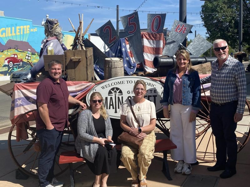 Members of the Wyoming Main Street Advisory Board gather together in from of a sign in downtown Gillette, Wyoming.
